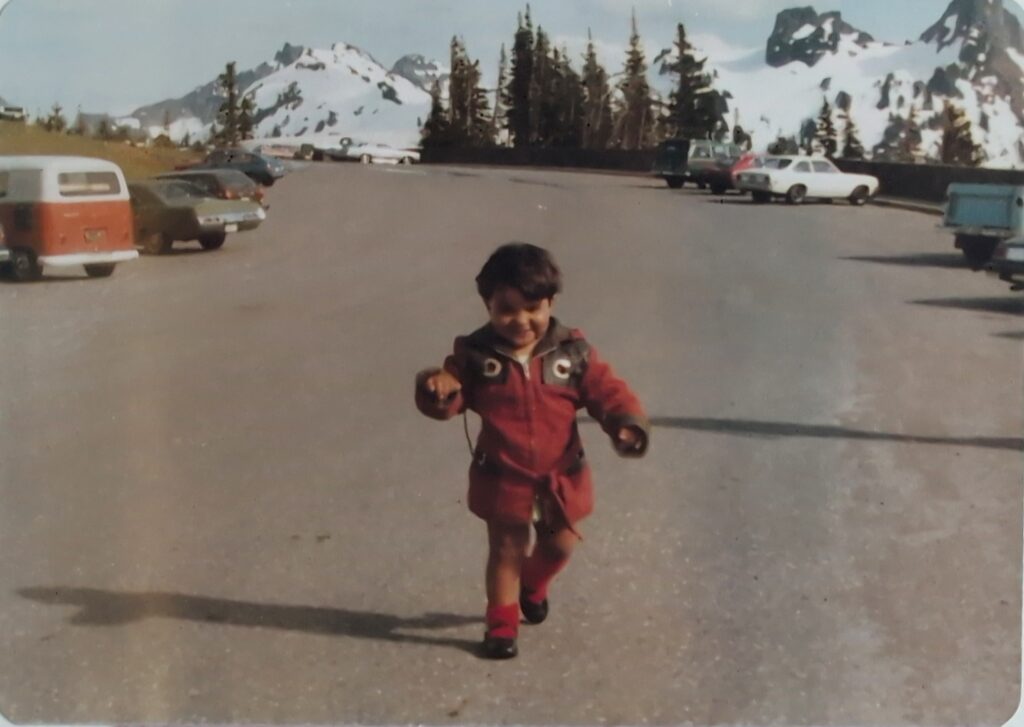 Young daughter walking in a Mount Rainier parking lot, red snowsuit